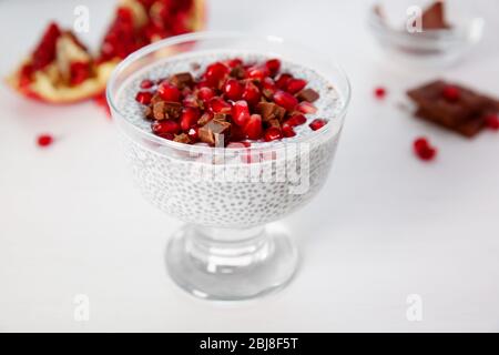 Budino di semi di Chia con granelli di melograno e patatine di cioccolato in piattino di vetro su fondo bianco Foto Stock