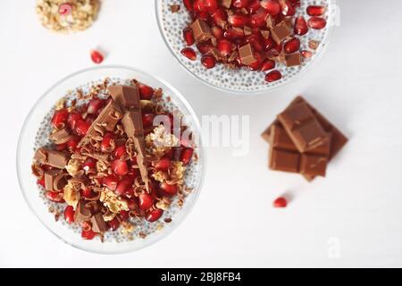 Vista dall'alto del budino di semi di chia con granelli di melograno e patatine di cioccolato in piattino di vetro su sfondo bianco Foto Stock