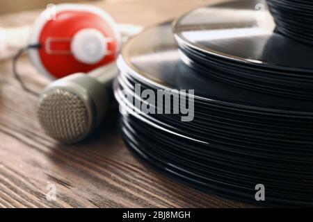 Pila di vecchi dischi in vinile con cuffie e microfono su sfondo in legno Foto Stock