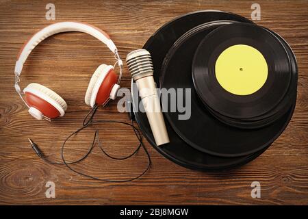 Pila di vecchi dischi in vinile con cuffie e microfono su sfondo in legno Foto Stock