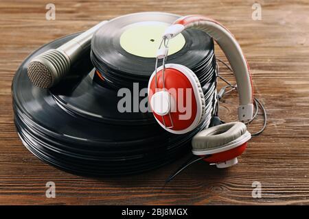 Pila di vecchi dischi in vinile con cuffie e microfono su sfondo in legno Foto Stock