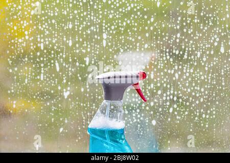 Detergente per vetri in una bottiglia di plastica con spray, sullo sfondo di una finestra. Lavavetro in blu. Primo piano. Foto Stock