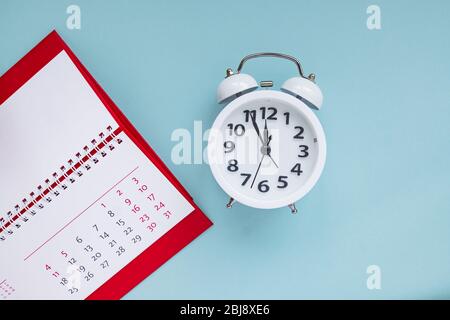 primo piano del calendario e sveglia su sfondo blu, pianificazione per meeting aziendali o pianificazione di viaggi. Foto Stock