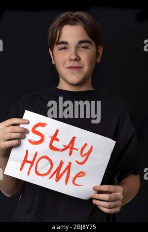 Un adolescente in una T-shirt nera si erge con l'iscrizione rimanere a casa. Tenendo un poster in lettere rosse rimanere a casa. Quarantena, coronavirus cavid19 Foto Stock