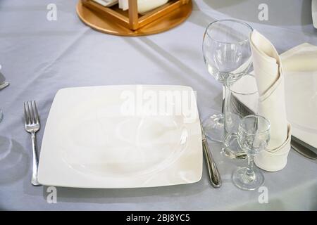 Il tavolo del ristorante è servito per cena. Su un tavolo con tovaglia bianca, bicchieri vuoti, piatti, tovaglioli. Messa a fuoco selettiva Foto Stock