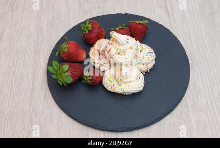 meringhe con fragole su piatto nero e fondo bianco Foto Stock