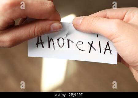 Mani femminili taglio pezzo di carta con anoressia parola Foto Stock
