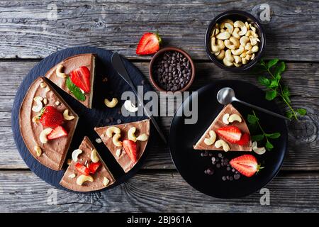 Torta al cioccolato triplo senza cottura a strati fatta di crema di cocco e fiocchi imbevuti con la crosta di datteri crudi, cacao e noci con fragole e menta Foto Stock