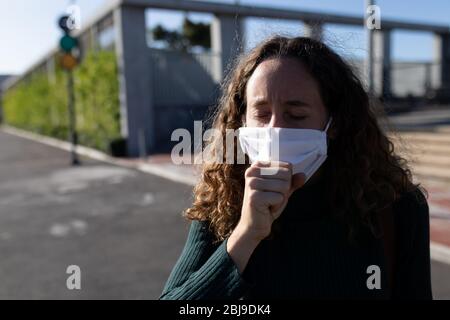 Donna caucasica che indossa una maschera protettiva e tosse fuori per le strade Foto Stock