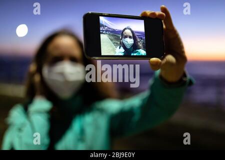 Donna caucasica che indossa una maschera protettiva contro il coronavirus, scattando una foto per le strade Foto Stock