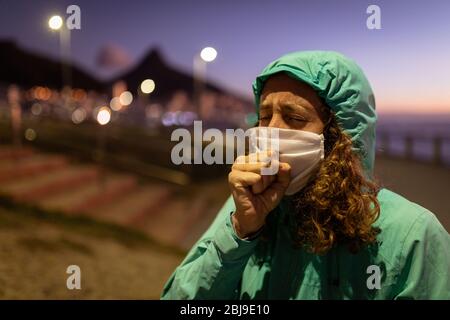 Donna caucasica che indossa una maschera protettiva contro il coronavirus, tossendo per le strade Foto Stock