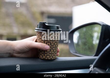 Mano della donna con una tazza di caffè, tè in macchina con la finestra aperta. Sicuro durante l'intiligent blocco nei Paesi Bassi. Finestra aperta, fuori m Foto Stock