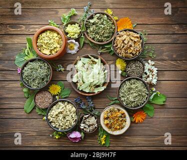 Selezione di erbe e fiori freschi in ciotole su sfondo di legno Foto Stock