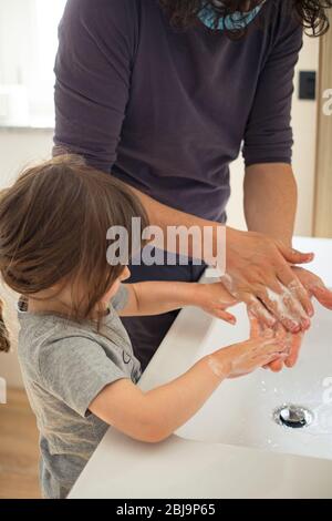 Padre caucasico indossare maschera facciale per evitare contagio insegnare bambina bambina come lavare le mani in bagno durante covid-19 pandemic blocco. Papà Foto Stock