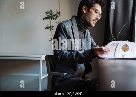 Immagine di un bel giovane uomo d'affari che indossa la tuta esaminando i documenti in bar Foto Stock