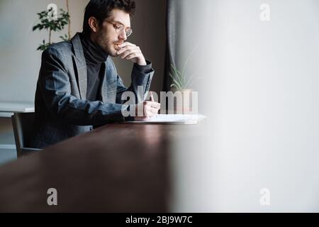 Immagine di un bel giovane uomo d'affari che indossa la tuta esaminando i documenti in bar Foto Stock