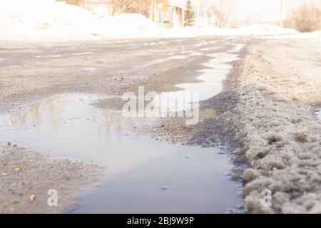 sfondo chiaro e pallido con ruscelli primaverili che scorrono lungo la strada ricoperta di ghiaccio e neve pesante, fuoco selettivo Foto Stock
