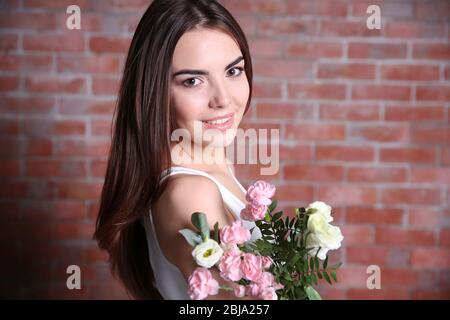 Bella giovane donna che tiene bouquet su sfondo muro di mattoni rossi Foto Stock