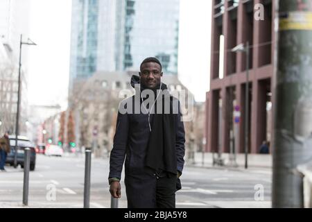 Giovane uomo nero che guarda Camera Walking su City Street Foto Stock