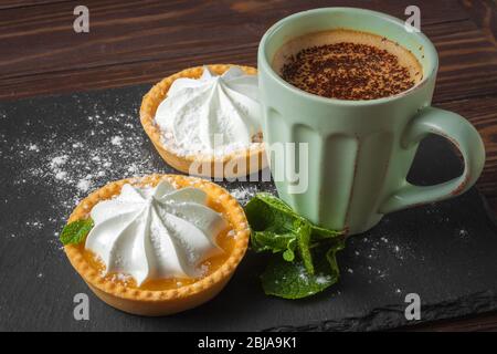 Crostata di limone con foglie di menta e una tazza di cappuccino con aggiunta di cioccolato. Foto Stock