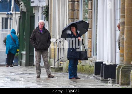 Bridport, Dorset, Regno Unito. 29 aprile 2020. Meteo Regno Unito. Gli amanti dello shopping con un ombrello per proteggersi dalla pioggia a Bridport a Dorset che fanno la fila fuori da una farmacia in una mattinata bagnata. Credito immagine: Graham Hunt/Alamy Live News Foto Stock