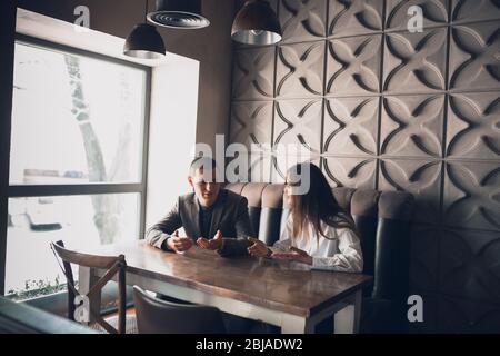 Un uomo allegro e una donna che parlano, discutono al bar, al bar. Coppia o amici, partner commerciali che lavorano toghether, seduti al tavolo in abbigliamento casual. Comunicazione, concetto di relazioni. Foto Stock