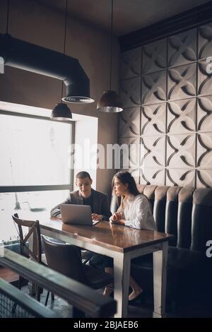 Un uomo allegro e una donna che parlano, discutono al bar, al bar. Coppia o amici, partner commerciali che lavorano toghether, seduti al tavolo in abbigliamento casual. Comunicazione, concetto di relazioni. Foto Stock