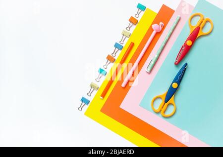 Fogli di carta colorata disposti in fila, pastelli, forbici e forniture su un tavolo bianco. Arte dei bambini, artigianato per i bambini o preparazione di un bambino per sc Foto Stock