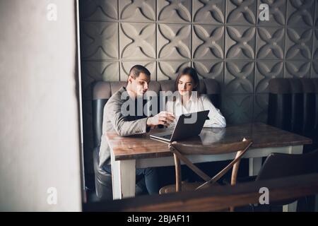 Un uomo allegro e una donna che parlano, discutono al bar, al bar. Coppia o amici, partner commerciali che lavorano toghether, seduti al tavolo in abbigliamento casual. Comunicazione, concetto di relazioni. Foto Stock