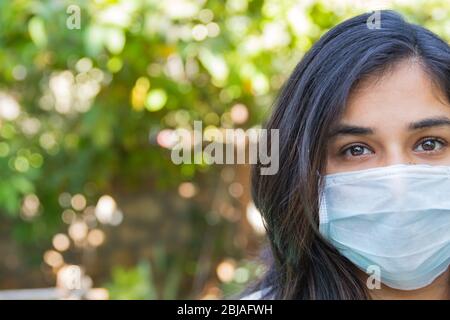 Ritratto a metà faccia di una ragazza indiana che indossa una maschera facciale durante la pandemia del covid 19 mentre il blocco continua in India a causa della crescente diffusione del coro Foto Stock