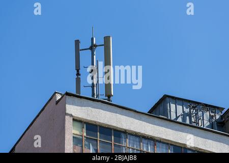 Antenna di comunicazione cellulare su un tetto piatto di un edificio di appartamenti a più piani contro il cielo blu in una giornata di sole. Vista ad angolo basso. Foto Stock