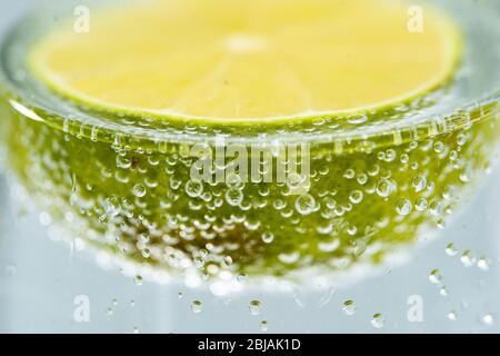 Calce fresca tagliata galleggiante in vetro soda con bolla su sfondo giallo. Fotografia commerciale sana di frutta. Foto Stock