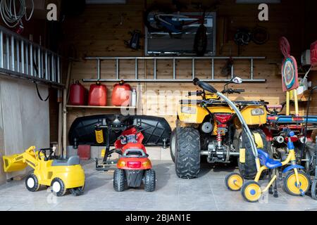 Vista interna porta aperta ATV quad moto parcheggio disordinato garage, cose ordine, giocattoli per bambini e deposito bicilce interno a casa. Magazzino della casa Foto Stock