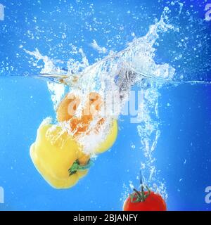 Gruppo di frutta e verdura fresca che cadono in acqua su sfondo blu Foto Stock