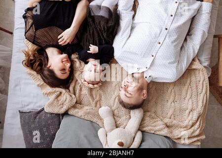 Bella giovane famiglia che si trova insieme sul letto a casa, mamma, papà e bambina, vista superiore. Giorno della madre, del padre, del bambino. Famiglia che trascorre tempo Foto Stock