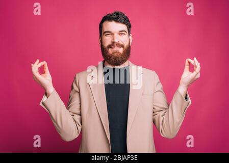 Giovane uomo bearded è in piedi in posa zen guardando la telecamera su sfondo rosa. Foto Stock