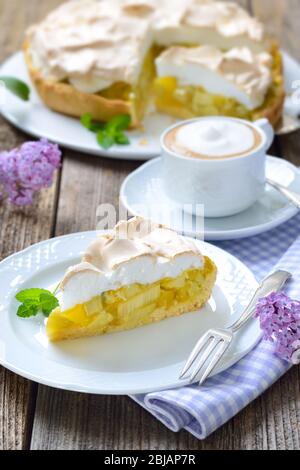 Deliziosa torta al rabarbaro con meringa dolce e una tazza di cappuccino servito su un tavolo di legno con decorazione lilla a forma di molla Foto Stock