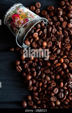 Chicchi fritti di fragrante caffè fresco sparsi da un secchio su un tavolo di legno Foto Stock