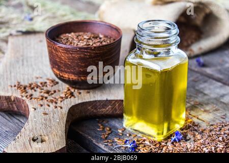 Olio di lino in un vaso vicino ai semi di lino su uno sfondo di vecchi assi. L'olio di semi di lino viene usato in cucina, medicina, cosmetologia. Foto Stock