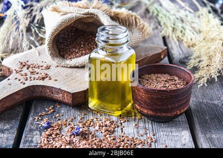 Olio di lino in un vaso vicino ai semi di lino su uno sfondo di vecchi assi. L'olio di semi di lino viene usato in cucina, medicina, cosmetologia. Foto Stock