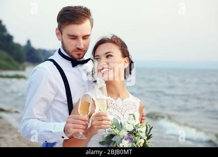 Sposo e sposa con bicchieri di champagne sulla riva del fiume Foto Stock