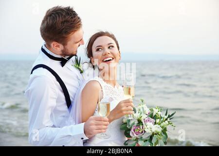 Sposo e sposa con bicchieri di champagne sulla riva del fiume Foto Stock