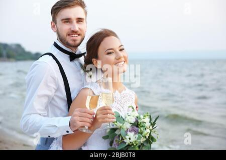 Sposo e sposa con bicchieri di champagne sulla riva del fiume Foto Stock