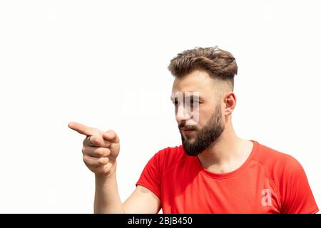 Vita su di giovane uomo bearded in rosso con espressione sprezzante e accusante, punta il dito a sinistra su qualcuno isolato su bianco Foto Stock