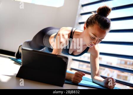 Attività di home work out online utilizzando servizi Internet con dispositivo tablet elettronico grazie al concetto di virus corona autoisolato. Donna in activewear eseguire asse Foto Stock