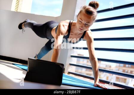 Attività di home work out online utilizzando servizi Internet con dispositivo tablet elettronico grazie al concetto di virus corona autoisolato. Donna in activewear eseguire asse Foto Stock