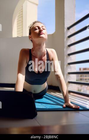 Donna indossare abbigliamento sportivo nero allenarsi in estate a casa a terrazzamento zona do yoga o pilates esercizio sul tappeto. Verso l'alto posa cane Urdhva mukha shvanasan Foto Stock