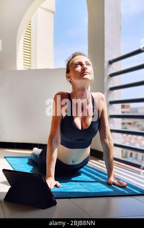 Donna indossare abbigliamento sportivo nero allenarsi in estate a casa a terrazzamento zona do yoga o pilates esercizio sul tappeto. Verso l'alto posa cane Urdhva mukha shvanasan Foto Stock