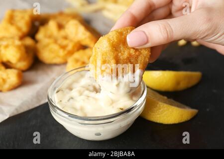 Donna che tiene gustoso pepino e ciotola con salsa sul tavolo, primo piano Foto Stock