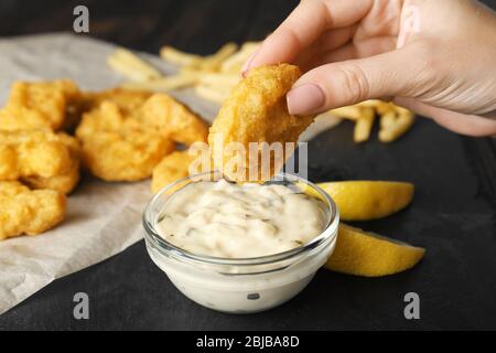 Donna che tiene gustoso pepino e ciotola con salsa sul tavolo, primo piano Foto Stock